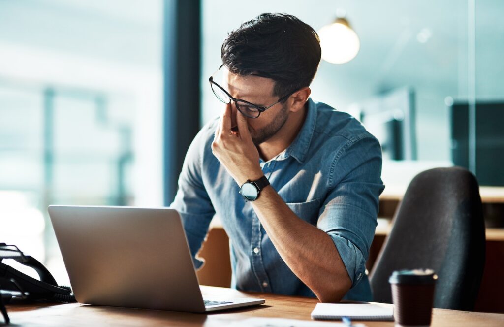 Project manager sitting at his desk rubbing his temples to indicate stress.